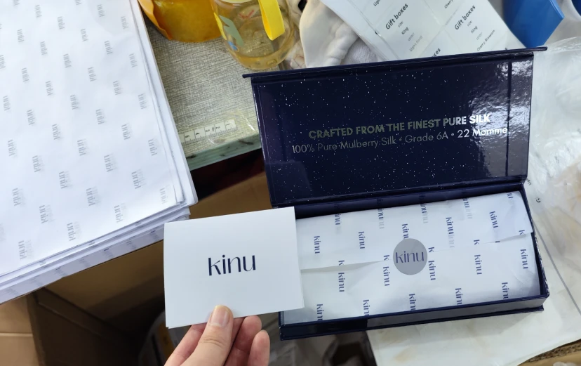 KINU-Geschenkset mit Seiden-Augenmaske und Haargummis, Markenkarte und Premium-Verpackung.
